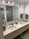 Dual-sink vanity featuring a light wood-finish cabinet with open shelving, a white surface, undermount rectangular sinks, and brushed metal hardware