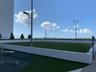 Outdoor recreation area featuring artificial turf, perimeter concrete walls, tall stadium-style lighting, and paved pathways