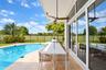 Covered lanai featuring natural stone flooring, ceiling fan, expansive glass sliding doors, private swimming pool, and wrought-iron style fencing