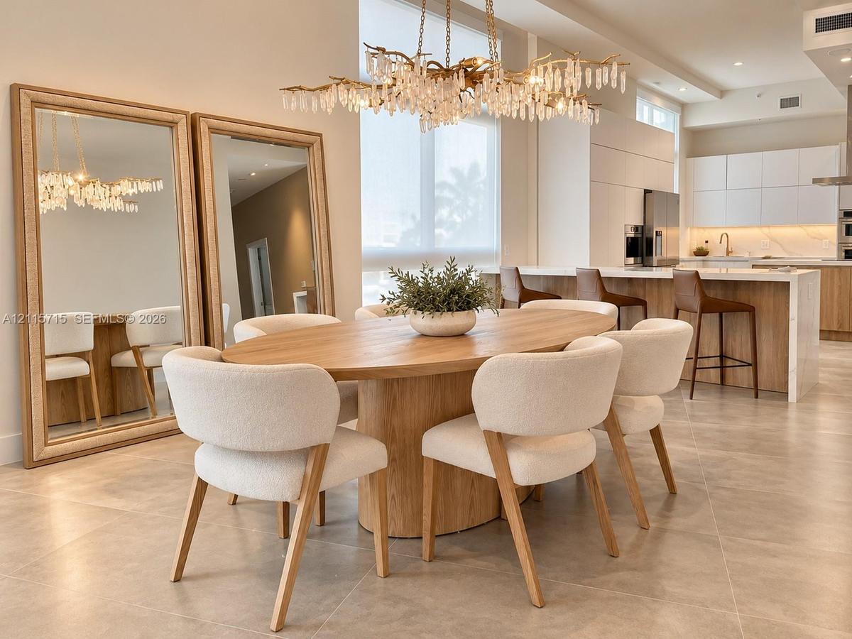 Open-concept interior featuring large-format tile flooring, a multi-tiered crystal statement chandelier, and a kitchen equipped with handleless flat-p