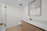 Guest full bathroom featuring a wood-finish vanity, solid surface countertop, brass-toned faucet and hardware, glass-enclosed shower with tiled surrou