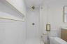 Walk-in shower with floor-to-ceiling white tile, recessed shelving with gold trim, brass fixtures, frameless glass door, and a two-piece toilet