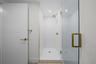Guest bathroom with walk-in shower featuring white tiled walls and floor, clear glass enclosure, brass-finish fixtures, and gold-toned trim accents