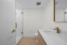 Guest bathroom featuring a walk-in shower with a glass enclosure, wood-finish flooring, vanity with a white countertop and integrated sink, brass-tone