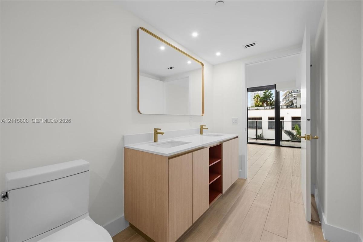 Master bathroom Dual-sink vanity with light wood cabinetry, white stone countertop, rectangular undermount sinks, and gold-tone fixtures, complemented