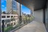 Covered balcony featuring wood-finish flooring, glass panel railing, and charcoal-tone metal framing