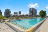 Rooftop swimming pool featuring a tiled basin, integrated step entry, textured perimeter decking, and stainless steel handrails