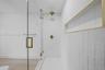 Walk-in shower featuring a frameless glass enclosure, gold-toned hardware, white wall tile, integrated recessed shelving, and a rain-style showerhead