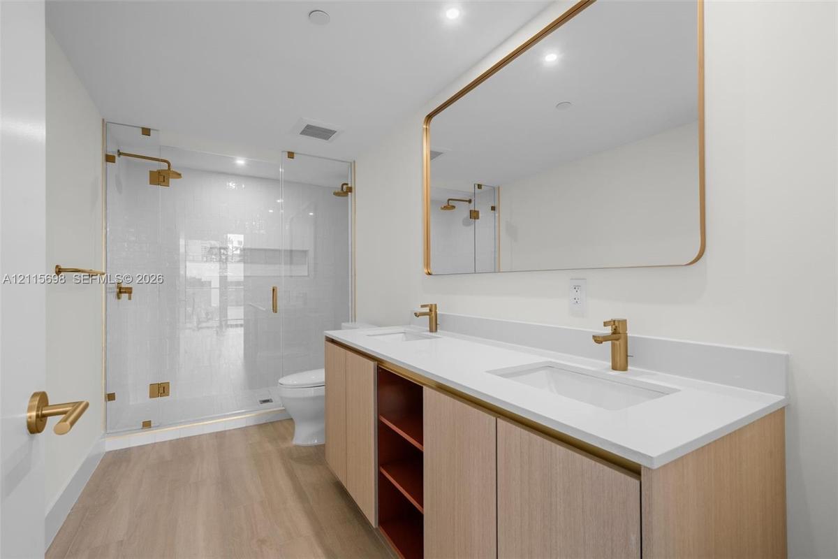 Master bathroom Dual-sink vanity with light wood cabinetry, white countertop, and gold-finish fixtures, complemented by a glass-enclosed walk-in showe