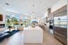 Open-concept interior featuring large center island with solid-surface countertop, linear wood-finish cabinetry, stainless steel built-in appliances, 