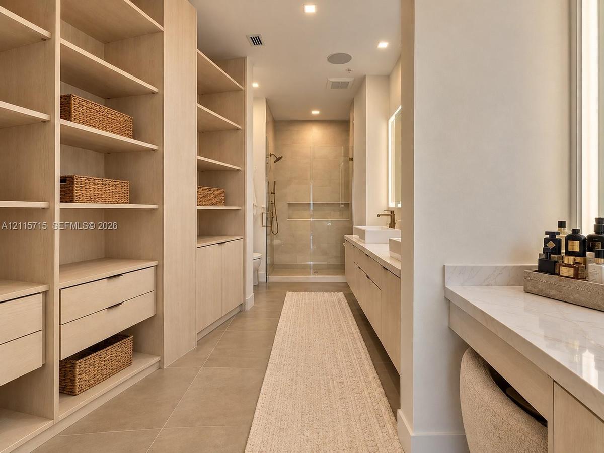 Custom built-in wood cabinetry, expansive walk-in storage, dual-sink vanity with stone countertop, frameless glass shower enclosure, and recessed ligh
