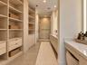 Custom built-in wood cabinetry, expansive walk-in storage, dual-sink vanity with stone countertop, frameless glass shower enclosure, and recessed ligh
