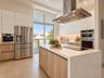Kitchen featuring a waterfall-edge stone island, built-in stainless steel appliances, flat-panel cabinetry, a stainless steel chimney range hood, and 