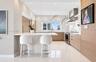 Kitchen featuring a waterfall-edge stone island, veined stone backsplash, stainless steel range hood, flat-panel wood-finish cabinetry, and recessed c