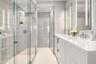 Walk-in glass-enclosed shower featuring large-format tile wall cladding, integrated wall niche, dual-sink vanity with white stone countertop, and vert