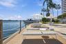 Waterfront deck featuring wood-finish decking, rope railing, stone-paved patio area, and mature palm trees