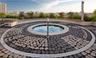 Circular in-ground spa featuring a stone-tiled deck, a smooth masonry surround, integrated perimeter lighting, and metallic handrail