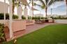 Outdoor terrace featuring wood-finish decking, integrated stainless steel grill station, synthetic turf lawn, architectural shade sails, and perimeter