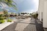 Expansive swimming pool area featuring a curved architectural overhang with structural columns, patterned stone masonry decking, and integrated plante