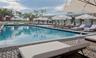 Expansive rectangular swimming pool featuring a pebble-tiled deck, metal handrails, and surrounding concrete pillars