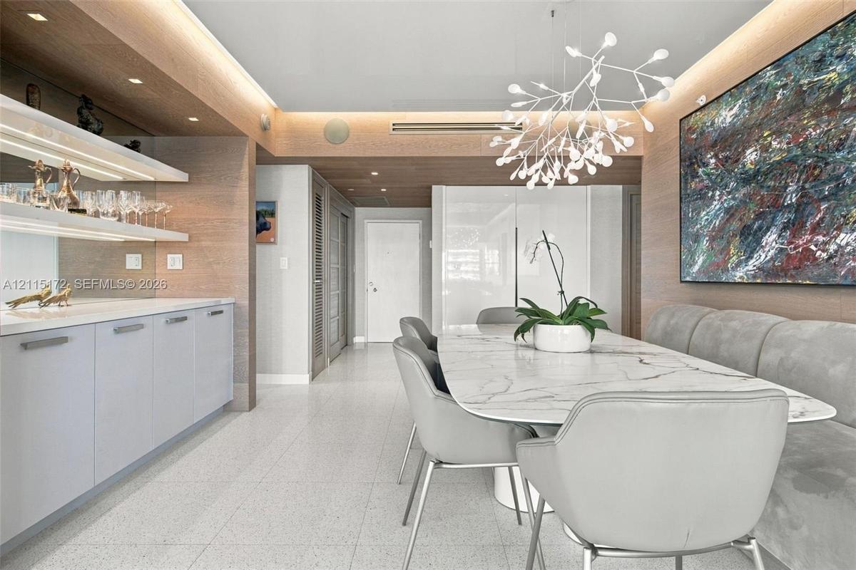 Built-in wet bar with illuminated shelving, integrated cabinetry, wood-finish wall paneling, ceiling recessed lighting, and a modern sculptural pendan