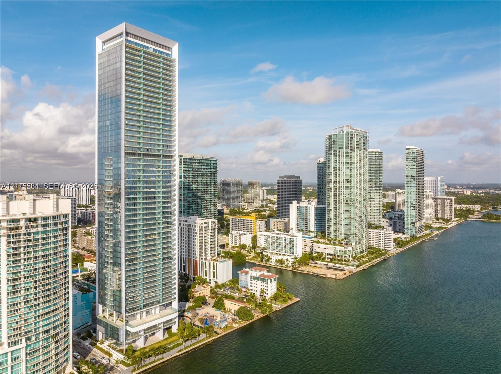 High-rise residential tower featuring a glass-curtain wall exterior, tiered architectural design, multiple private balconies, and a prominent waterfro