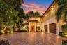 Mediterranean-style exterior featuring a clay tile roof, dual-entry wood doors, paver driveway, and a gated entry with perimeter landscaping