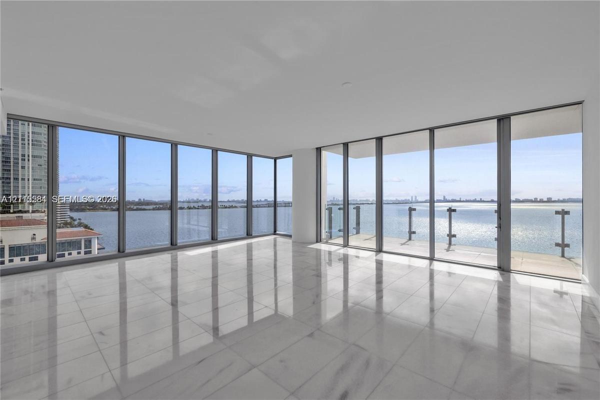 Floor-to-ceiling windows, wrap-around glass balcony railing, expansive stone tile flooring, and panoramic water exposure