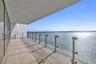 Covered balcony with large-format tile flooring and floor-to-ceiling glass wall panels, featuring a frameless glass railing with metal posts