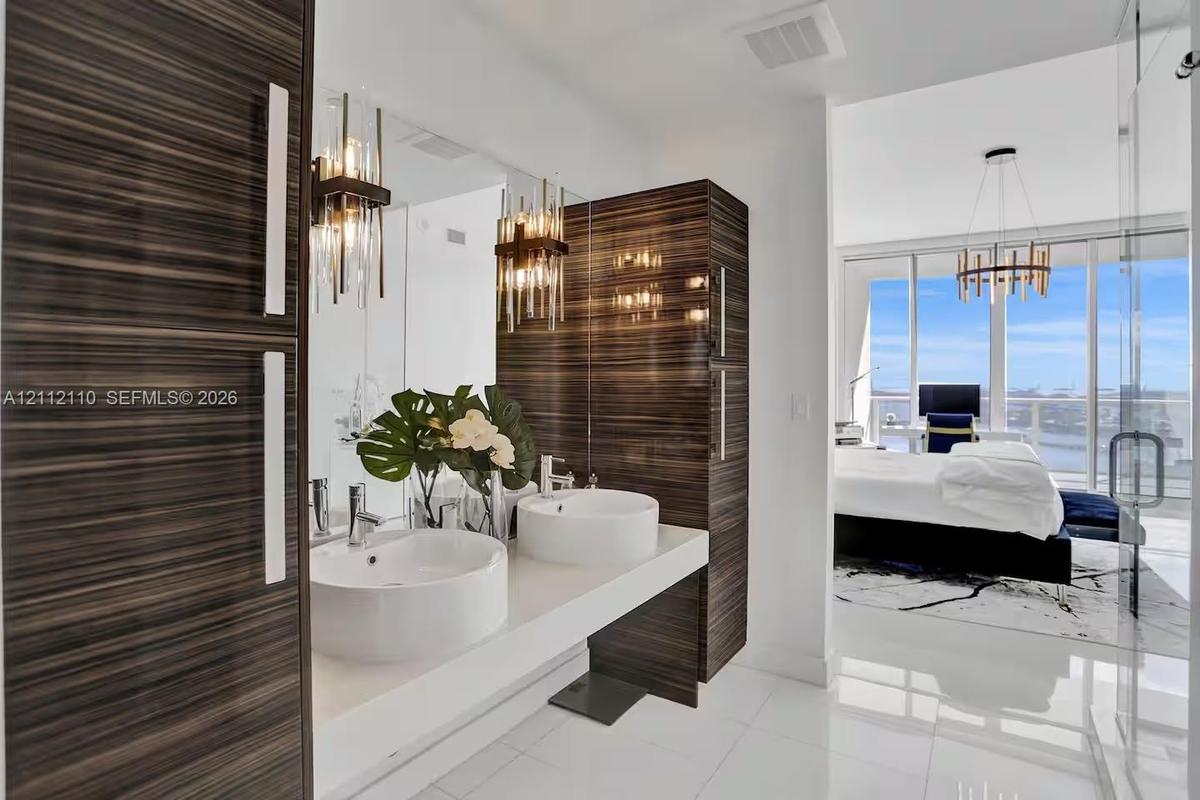 Floating vanity with dual vessel sinks, high-gloss horizontal wood-grain cabinetry, polished stone countertop, and statement vertical pendant lighting