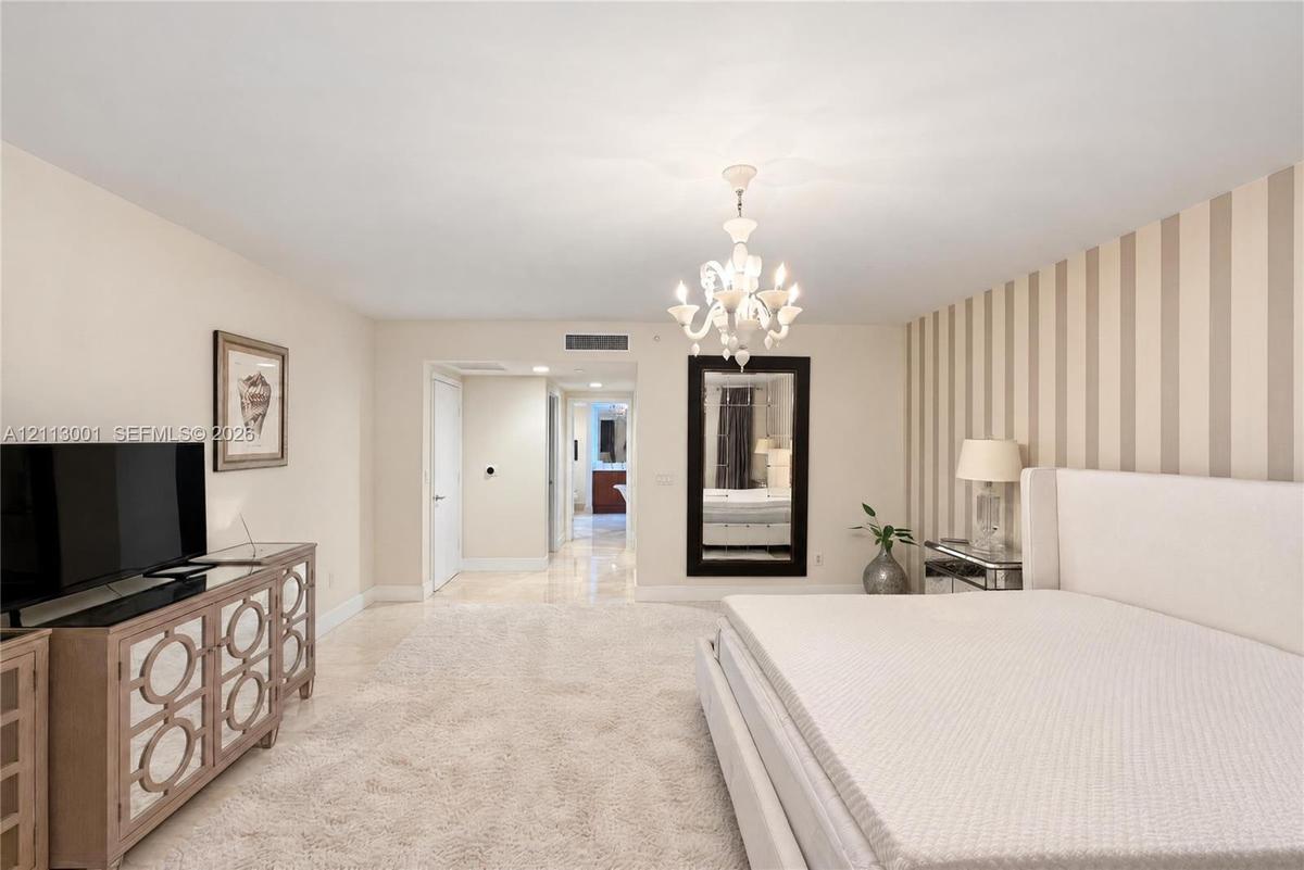 Spacious interior featuring a multi-arm crystal chandelier, wall-to-wall carpeting, and an accent wall with vertical striped wallcovering
