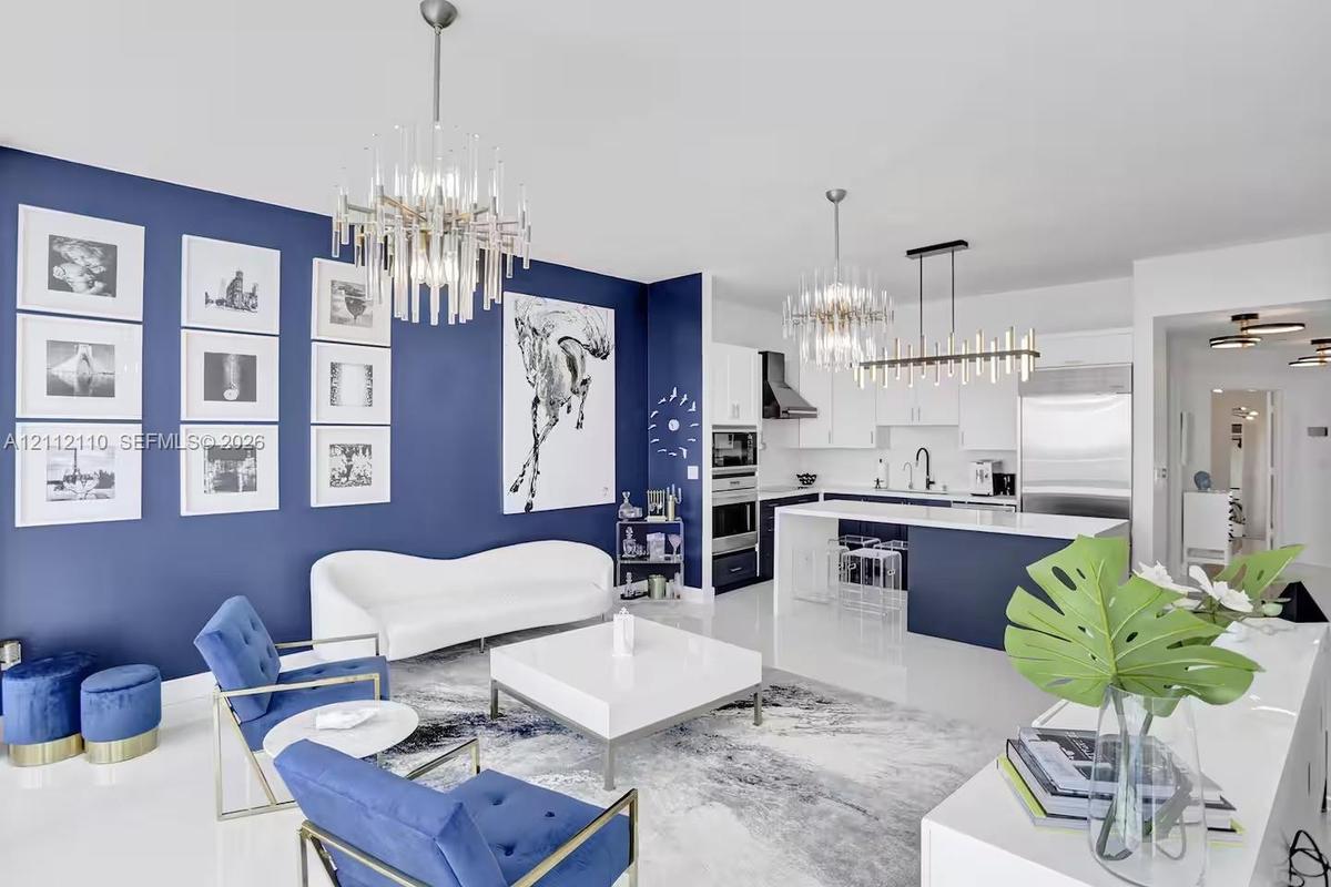 Open-concept living space featuring high-gloss flooring, tiered crystal chandeliers, two-tone custom cabinetry, a stone-topped kitchen island, and a d