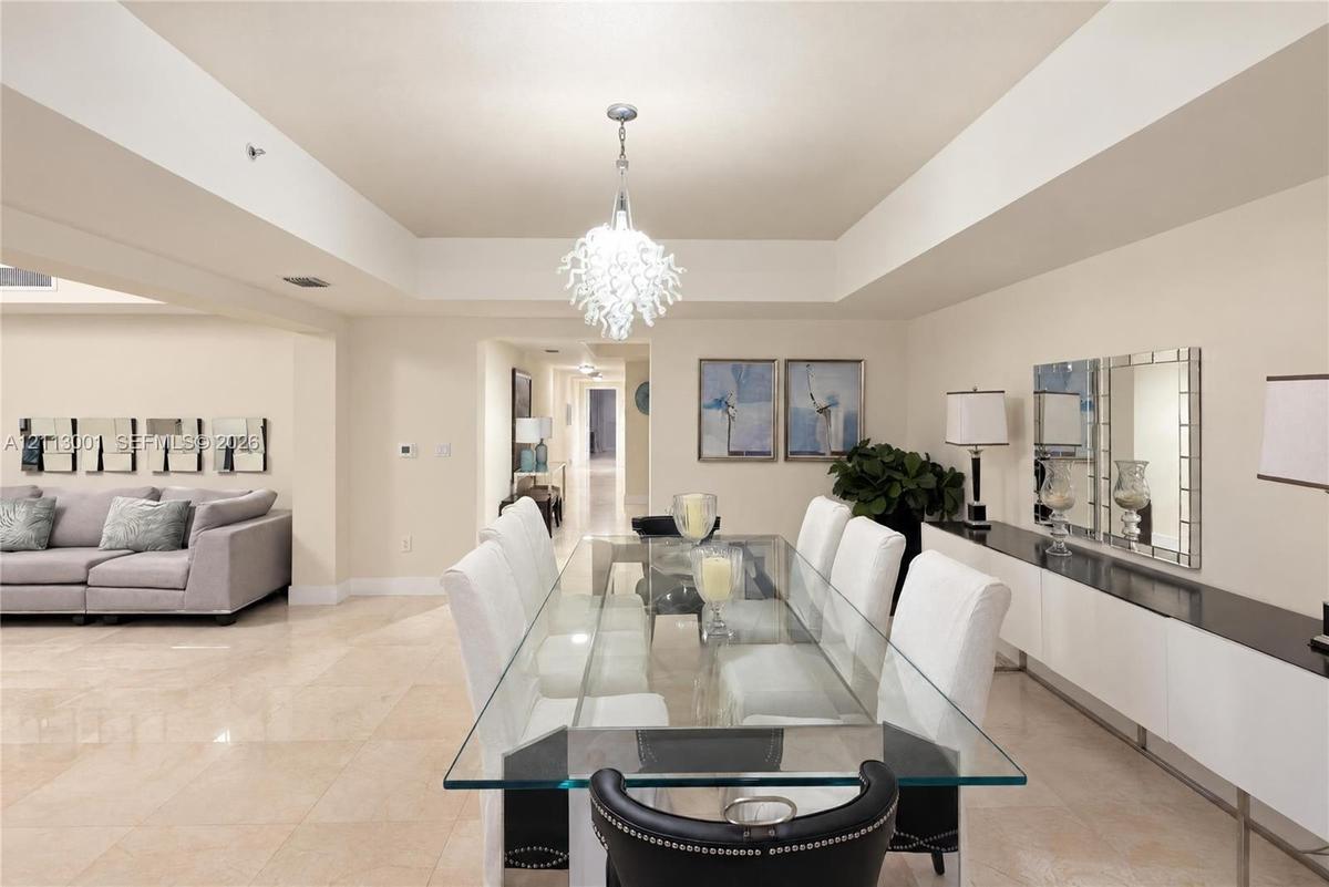Open-concept living space featuring high tray ceilings, polished tile flooring, a multi-tiered crystal chandelier, and a built-in wall-mounted buffet 