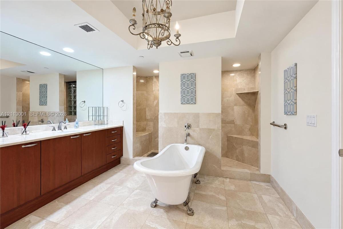 Freestanding soaking tub with claw feet, tile-surround walk-in shower with built-in bench, dual-sink vanity with light-toned countertop, and iron chan