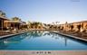 Rectangular swimming pool featuring a stone-tiled deck, metal handrails, integrated pool lighting, and surrounding covered structures with architectur