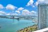 High-rise building with a prominent glass-paneled balcony railing, overlooking a coastal expanse featuring bridges, a waterway, and urban skyline scen