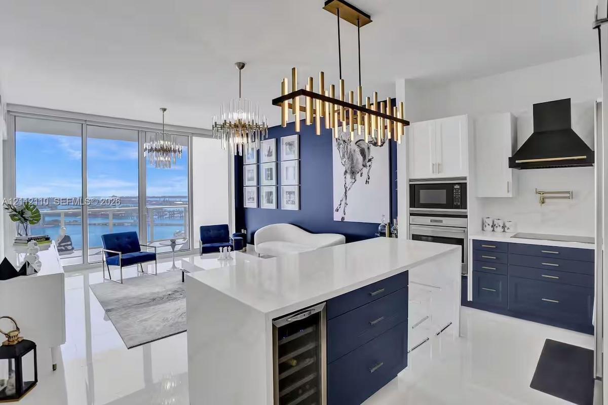 Kitchen featuring a stone-topped island with built-in wine cooler, custom navy and white cabinetry, integrated stainless steel appliances, wall-mounte