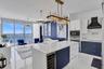 Kitchen featuring a stone-topped island with built-in wine cooler, custom navy and white cabinetry, integrated stainless steel appliances, wall-mounte