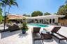 Backyard featuring a custom-shaped swimming pool, extensive light-toned stone hardscaping, multiple glass French door entries, and mature tropical pal