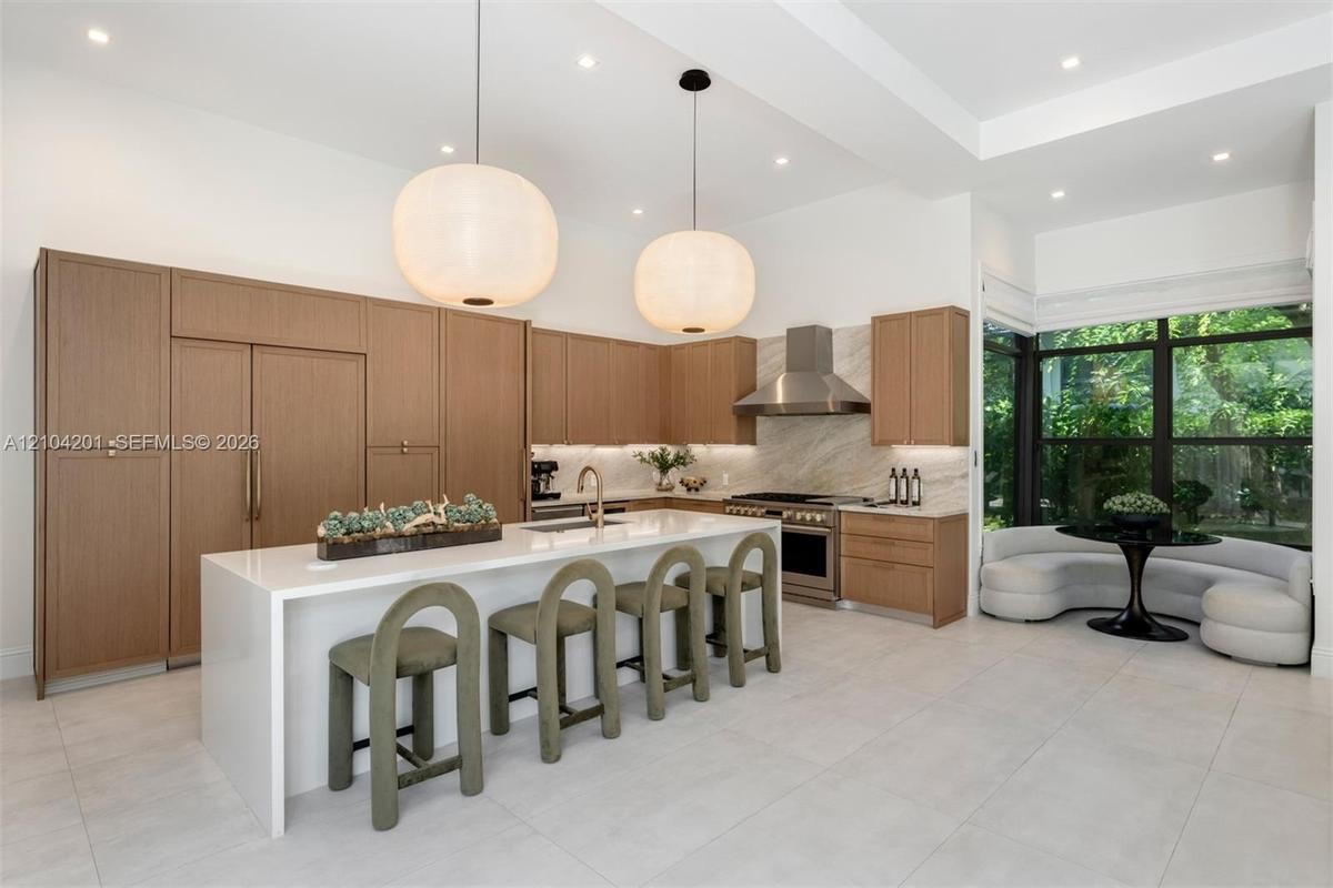 Kitchen featuring flat-panel wood cabinetry, large waterfall-edge island, stone-surround range hood, integrated stainless steel appliances, and large-