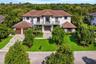Two-story stucco exterior featuring a multi-hipped tile roof, balcony with decorative metal railings, paver driveway, and multiple double-door entries