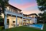 Two-story stucco exterior featuring a covered patio, upper-level balcony with decorative railing, rectangular swimming pool with stone coping, and mat