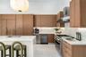 Kitchen featuring wood cabinetry, white stone countertops, integrated stainless steel appliances, a stainless steel range hood, and a large central is