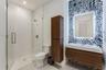 Bathroom featuring a walk-in shower with a frameless glass enclosure, wall-mounted wood-finish vanity, illuminated mirror, decorative patterned wall t