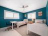 Bedroom featuring white plantation shutters, polished tile flooring, and a ceiling-mounted light and fan fixture