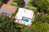 Aerial perspective of a property featuring a white metal roof, an in-ground swimming pool, a concrete patio, and extensive mature tree canopy