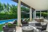 Covered outdoor patio featuring light stone flooring, structural columns with horizontal slat accents, built-in outdoor kitchen, swimming pool, and ma