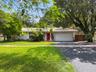 Single-story residence featuring a tile roof, paved driveway, two-car garage, and established mature trees