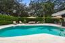 Curved swimming pool with built-in stairs, large-format stone paver decking, and extensive mature privacy hedging