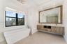 Freestanding soaking tub with chrome floor-mounted faucet, wall-mounted wood-finish vanity with dual undermount sinks, stone-surface countertop, and o